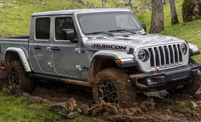 The 2023 Jeep Gladiator Rubicon being driven on a muddy trail, its wheels and lower body spattered with mud