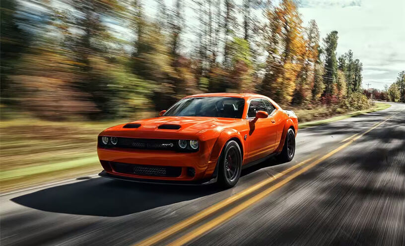 An orange 2023 Dodge Challenger SRT Super Stock being driven on a highway with the background blurred to indicate the speed of the vehicle.